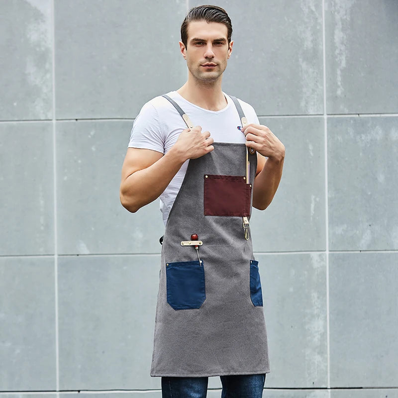 Man wearing a gray apron with a blue pocket against a gray tiled wall.